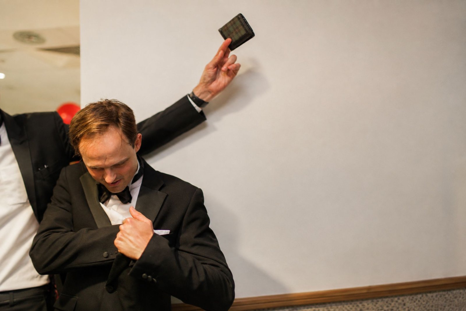 Guest checking his jacket pocket while the magician holds his wallet up behind him